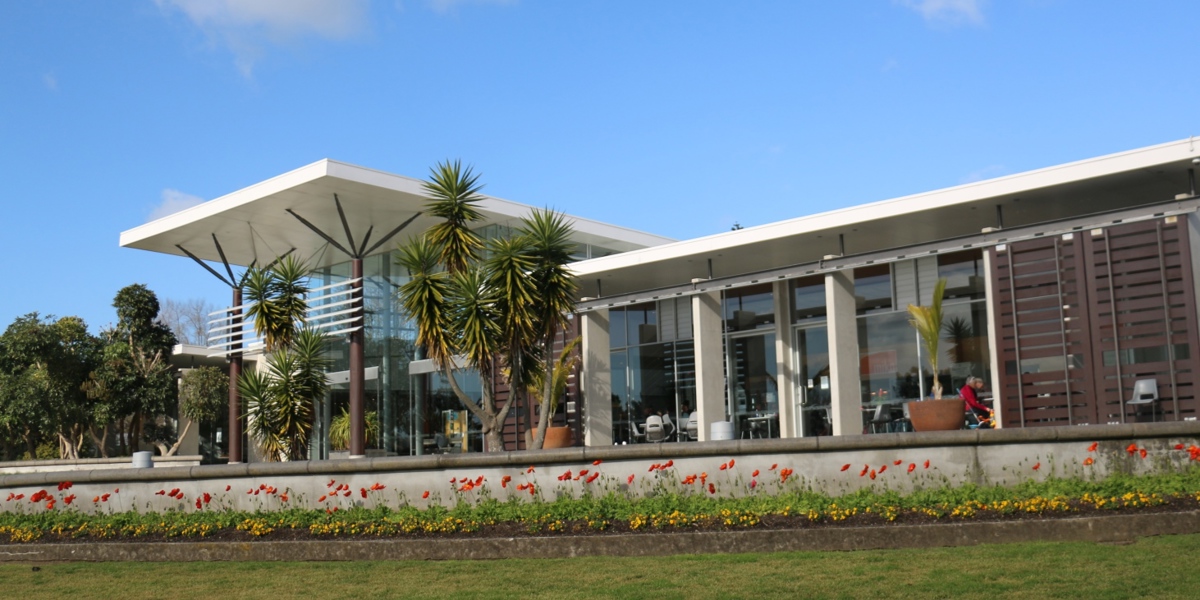 The image shows the visitor centre terrace on a sunny day with chairs and tables under the eaves set up for customers of cafe Miko. The blooms of red poppies adorn the foreground below the terrace.