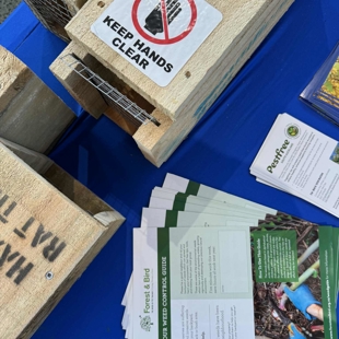  Image shows wooden pest traps with a sticker on top saying 'keep hands clear' alongside some brochures from Forest and Bird.